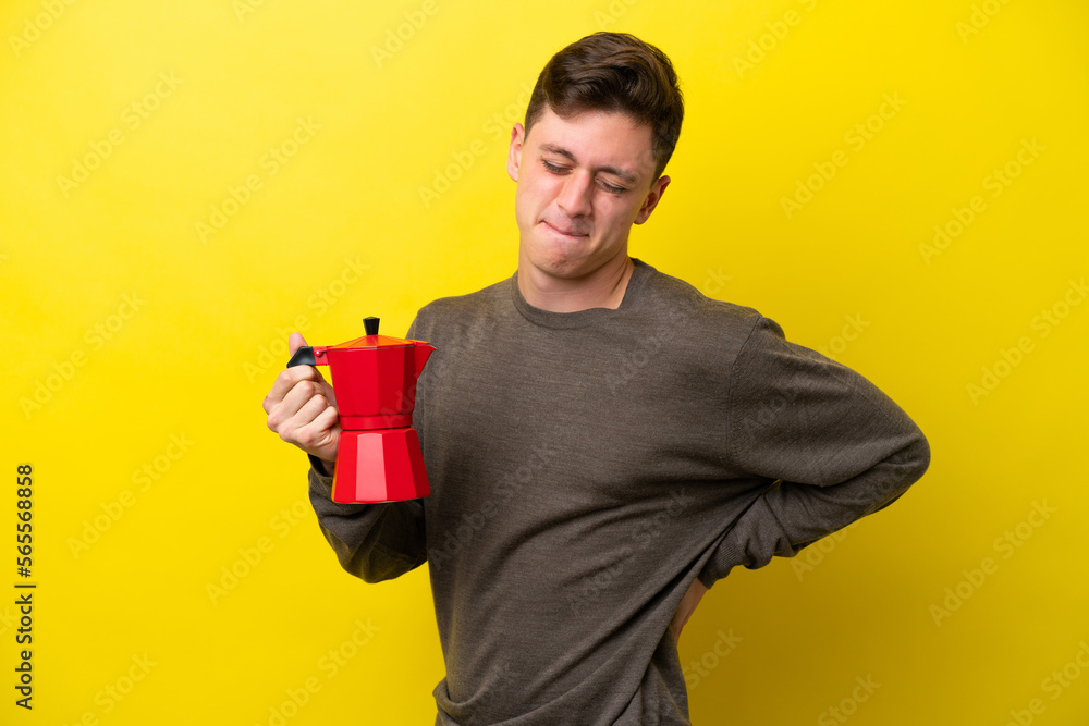 Young Brazilian man holding coffee pot isolated on yellow background suffering from backache for having made an effort Young Brazilian man holding coffee pot isolated on yellow background suffering from backache for having made an effort