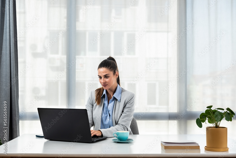 Young happy professional business woman employee sitting at desk working on laptop in modern corporate office interior. Smiling female worker using computer technology typing browsing web Young happy professional business woman employee sitting at desk working on laptop in modern corporate office interior. Smiling female worker using computer technology typing browsing web