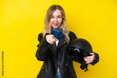 Blonde English young girl with a motorcycle helmet isolated on yellow background surprised and pointing front