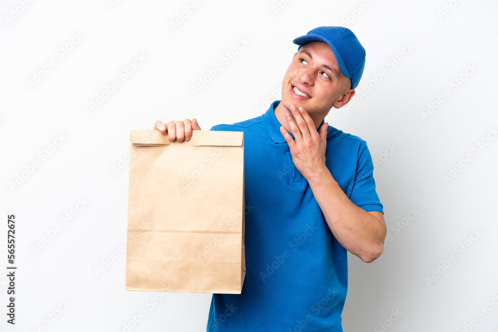 Young Brazilian man taking a bag of takeaway food isolated on white background looking up while smiling Young Brazilian man taking a bag of takeaway food isolated on white background looking up while smiling