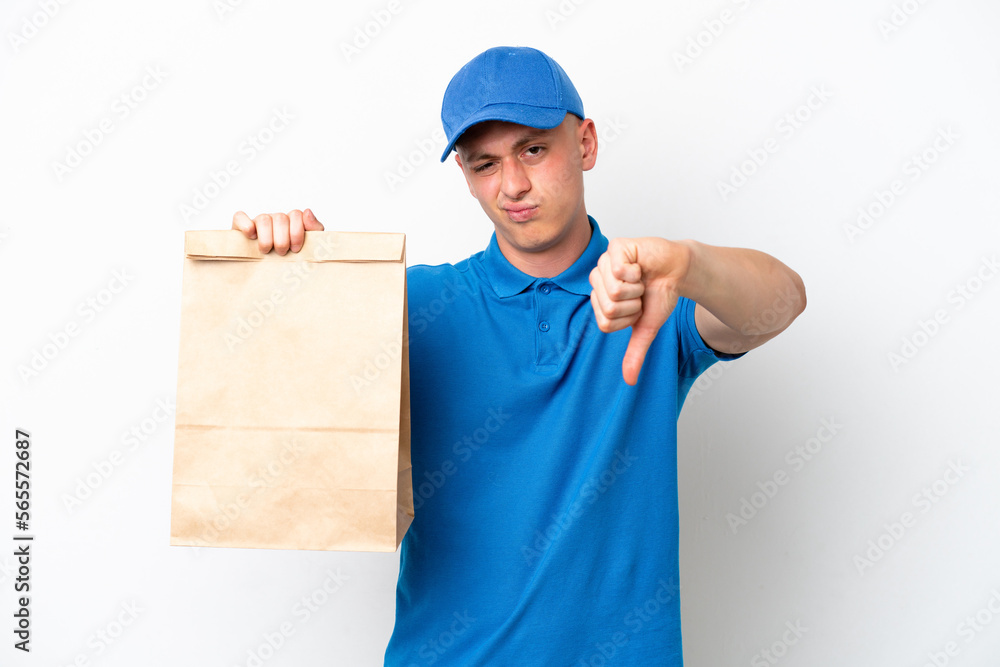 Young Brazilian man taking a bag of takeaway food isolated on white background showing thumb down with negative expression Young Brazilian man taking a bag of takeaway food isolated on white background showing thumb down with negative expression
