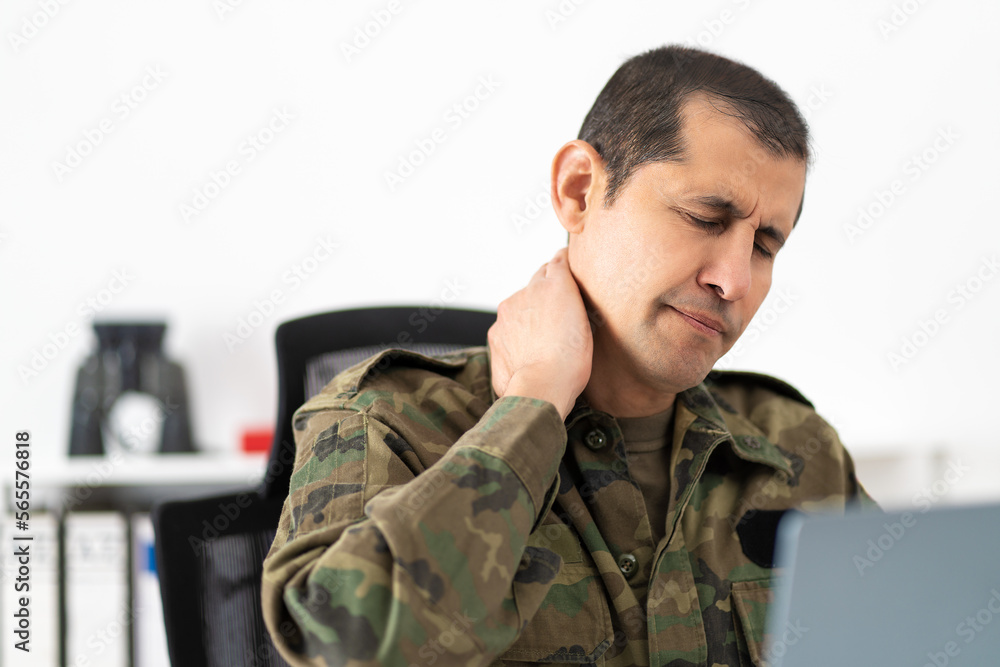 Shot of a mid adult male soldier experiencing discomfort in his shoulders while sitting at his desk Shot of a mid adult male soldier experiencing discomfort in his shoulders while sitting at his desk