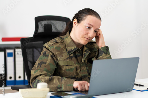 Female soldier with a stress headache feeling tired, pain and stressed while working on a computer.Unhealthy female soldier with stomach ache with her hand on her head in the office