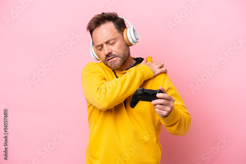 Middle age man playing with a video game controller isolated on pink background suffering from pain in shoulder for having made an effort