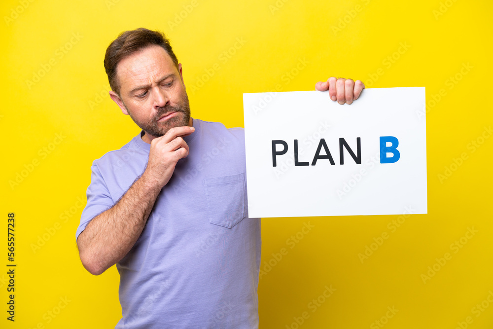 Middle age caucasian man isolated on yellow background holding a placard with the message PLAN B and thinking Middle age caucasian man isolated on yellow background holding a placard with the message PLAN B and thinking