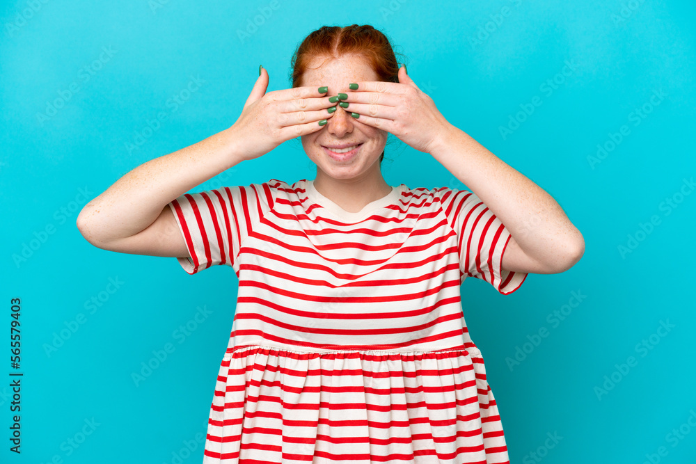 Young reddish woman isolated on blue background covering eyes by hands and smiling Young reddish woman isolated on blue background covering eyes by hands and smiling