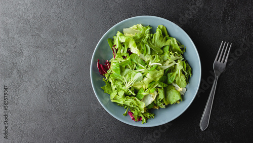 Green salad leaves in bowl on black table.