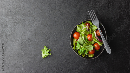 Green salad leaves in bowl on black table.