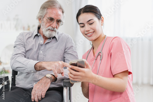 Beautiful nurse take care old caucasian man of use smartphone at home 