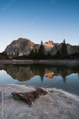 Dämmerung in den bergen an einem See mit einem Ast und dem ersten Sonnenlicht auf den Bergspitzen in den Dolomiten.