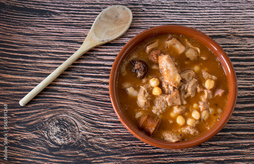 Cazuela de callos con garbanzos con una cuchara de madera sobre mesa de madera rústica. Cazuela de callos con garbanzos con una cuchara de madera sobre mesa de madera rústica.
