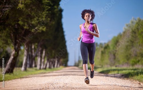 A woman runs on a dirt road lined with trees. photo