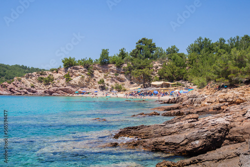 Sand beach surround rocks and pine trees with people enjoying summer vacation, turquoise color clear sea. Holiday and travel concept.