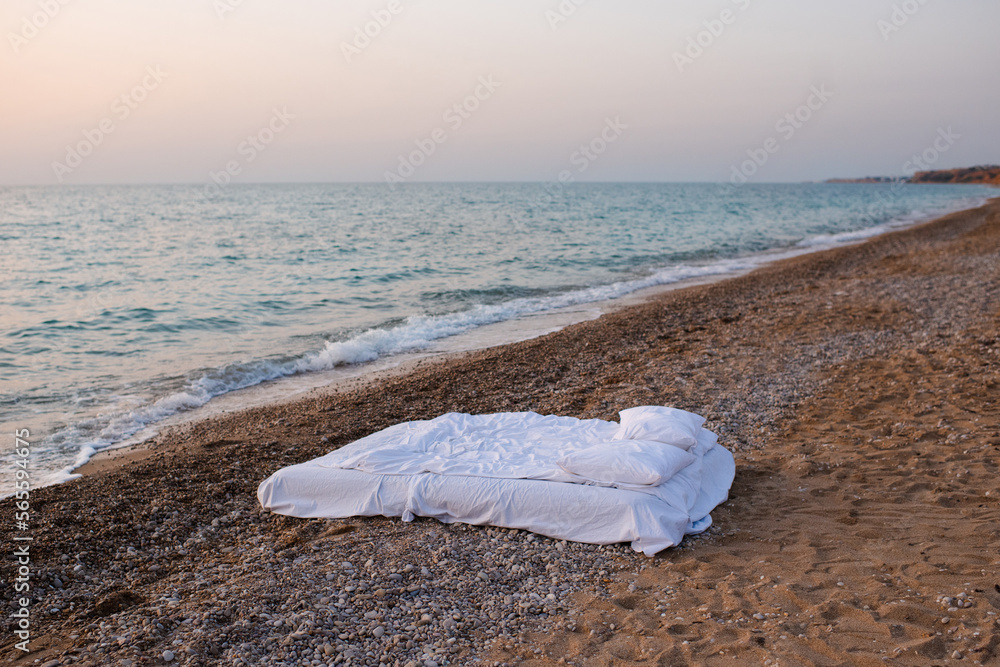 Bed with white duvet and pillows at beach with sea background over sunrise outdoor. Summer vacation season. Bed with white duvet and pillows at beach with sea background over sunrise outdoor. Summer vacation season.