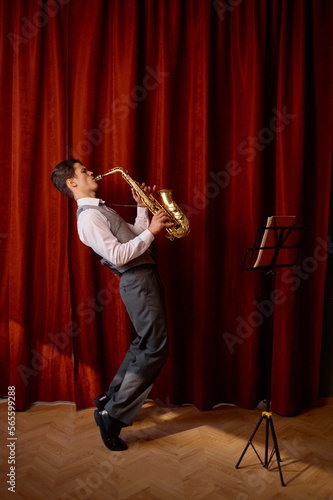 Εκτύπωση καμβά Young musician plays tenor saxophone on stage with red drape curtains