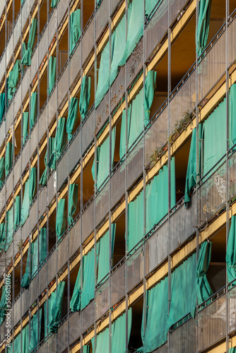Multi-storey building with rows of balconies in Barcelona. Yellow facade with green, old fashioned shades.