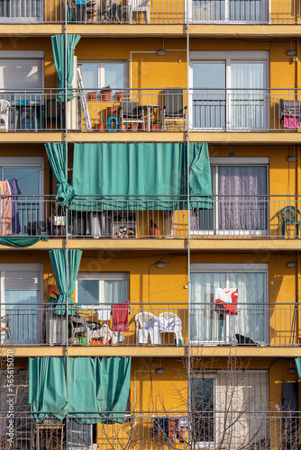 Multi-storey building with rows of balconies in Barcelona. Yellow facade with green, old fashioned shades.