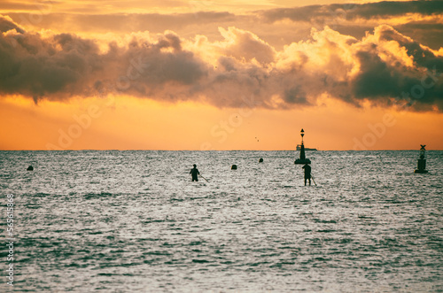 Silhouette of people doing stand up paddle at sunrise © Cristina