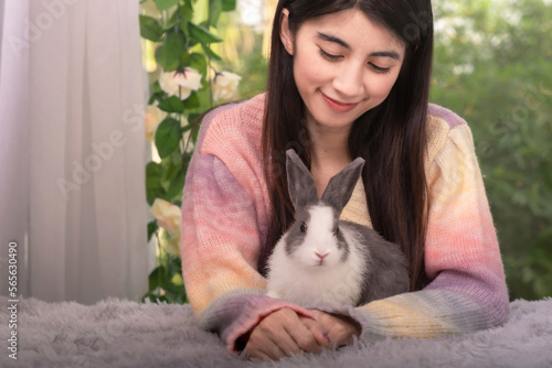 Beautiful asian woman with sweet sweater embrass her fluffy rabbit with smile of hapiness and love, taking care of pet, relationship between human and pet concept. photo