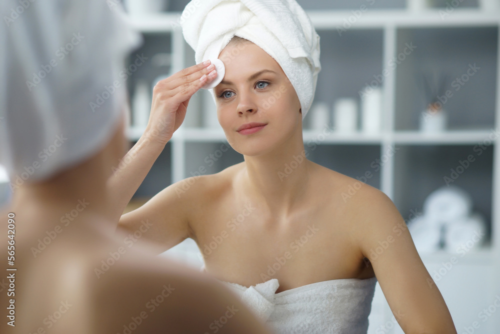 Young woman sits in the bathroom in front of the makeup mirror and does cosmetic procedures. Beautiful girl in white towel. Skin care, health, rejuvenation and spa treatment concept. Young woman sits in the bathroom in front of the makeup mirror and does cosmetic procedures. Beautiful girl in white towel. Skin care, health, rejuvenation and spa treatment concept.