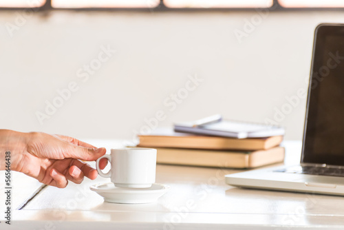 delicate hand lifting a white coffee cup, a laptop computer, office breakfast