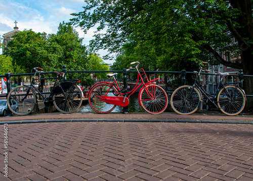 A red bicycle between two other bicycles over a canal in Amsterdam during the Summer