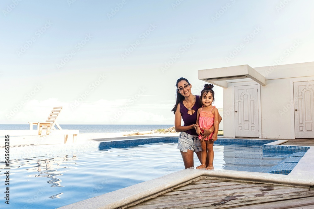 Young hispanic mother with baby daughter together in swimming pool.