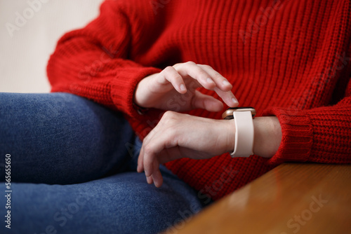 Young girl browsing notifications on smart wrist watches. Female person sitting on couch at home and using modern smartwatches