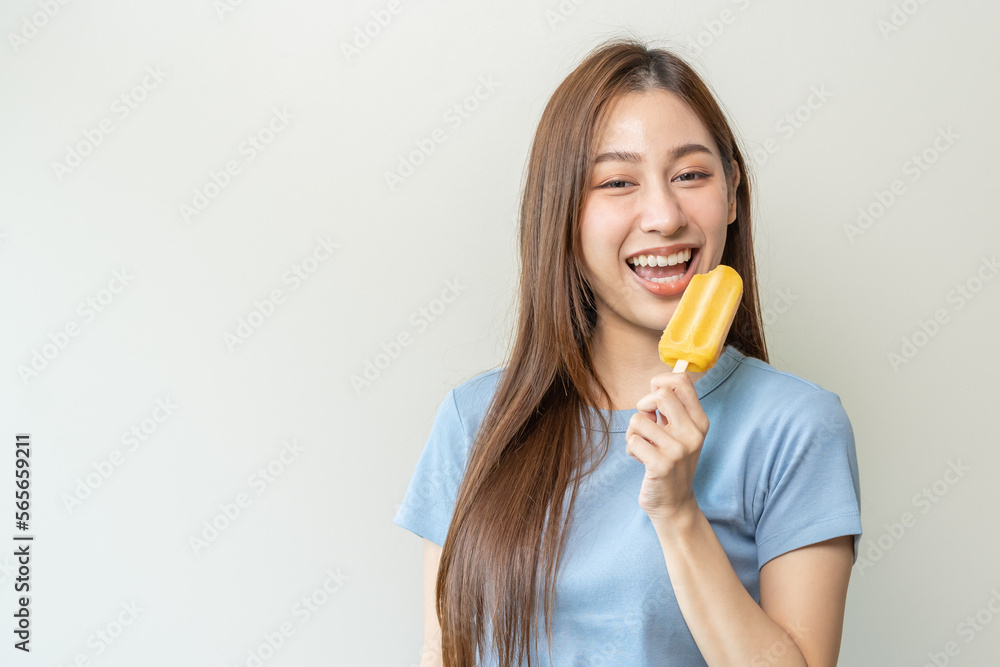 Cheerful enjoy, happy cute asian woman wearing casual with brunette hair, eating popsicle, teenage girl holding ice pop, lolly frozen stick with mango yellow, passion fruit ice cream tasty in summer. Cheerful enjoy, happy cute asian woman wearing casual with brunette hair, eating popsicle, teenage girl holding ice pop, lolly frozen stick with mango yellow, passion fruit ice cream tasty in summer.
