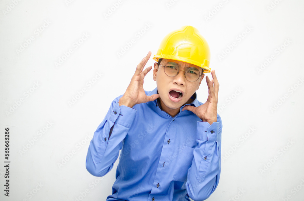 asian male construction worker or engineer in blue shirt and safety yellow helmet shows expresion of anger, furious and dissapointment isolated over white. stressed over work concept asian male construction worker or engineer in blue shirt and safety yellow helmet shows expresion of anger, furious and dissapointment isolated over white. stressed over work concept