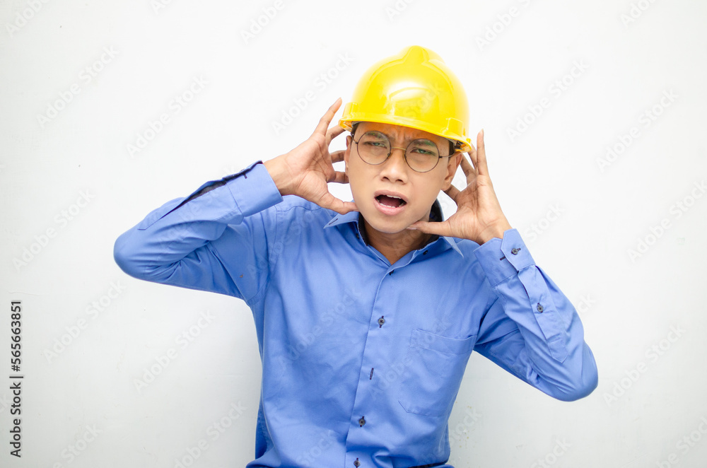 asian male construction worker or engineer in blue shirt and safety yellow helmet shows expresion of anger, furious and dissapointment isolated over white. stressed over work concept asian male construction worker or engineer in blue shirt and safety yellow helmet shows expresion of anger, furious and dissapointment isolated over white. stressed over work concept