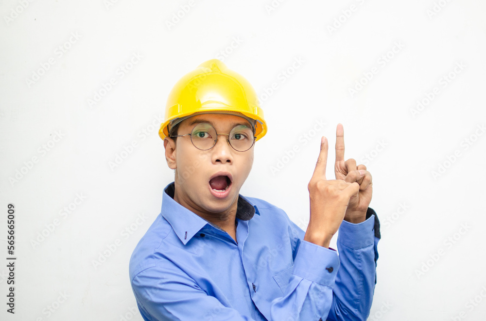 side view of A happy, shocked asian consrtuction worker in blue shirt and yellow safety helmet pointing finger and presenting something ads. 
