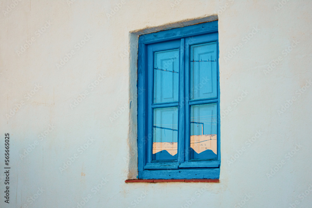 Old blue wooden window with the reflection of the sunset on a white wall