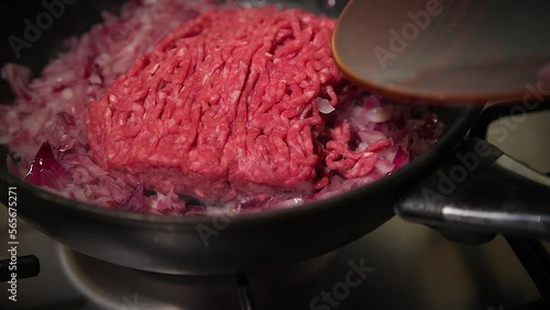 adding raw  ground beef into the frying pan and sauteing it with chopped red onions on the stove