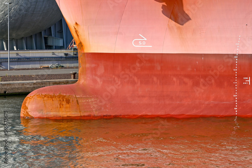 Close up view of the bulbous bow of a large cargo ship with painted markings on the side to indicate its depth in the water. No people.