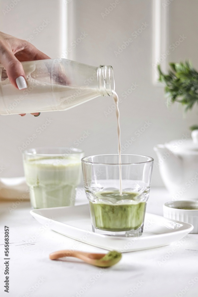 Person pouring matcha latte into a glass on the white background 