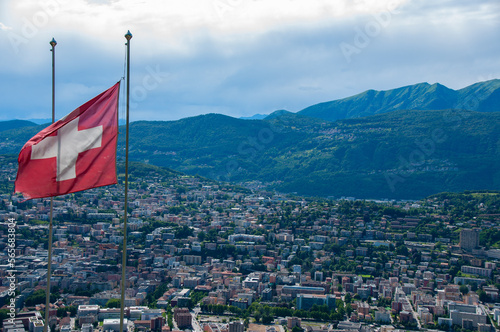 The Swiss flag in the foreground and the town of Lugano in the background in the Valley of the Swiss Alps