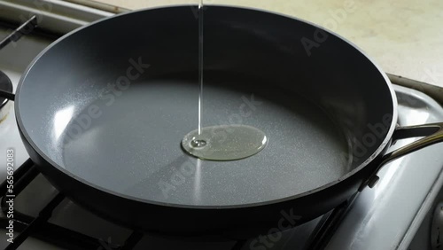 Rapeseed oil is poured into a grey non-stick frying pan on the stove. photo