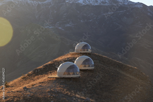 Wavy slopes of mountains overgrown with dry grass and white spherical camping houses - on a sunny winter day in the mountains of Dagestan.