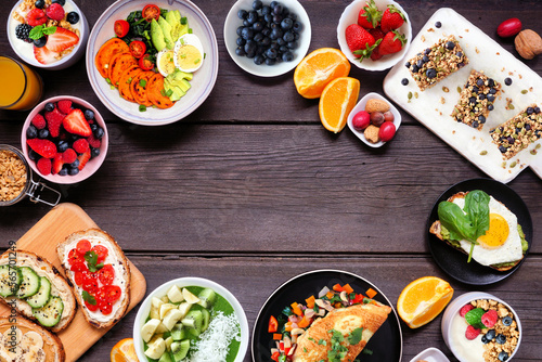 Healthy breakfast food frame. Top view over a dark wood banner background. Table scene with omelette, nutritious bowl, toasts, granola bars, smoothie bowl, yogurts, fruit. Copy space.