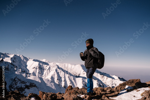 a guy with a cup of coffee stands high in the mountains and looks into the distance