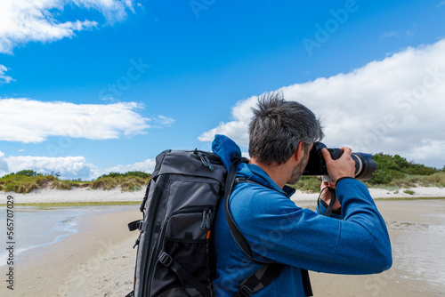 man with backpack takes photos on sandy beach