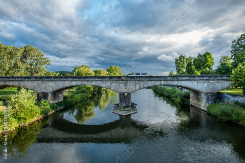 Steinbrücke mit Spiegelung in Flusss mit dramatischem Wolkenhimmel