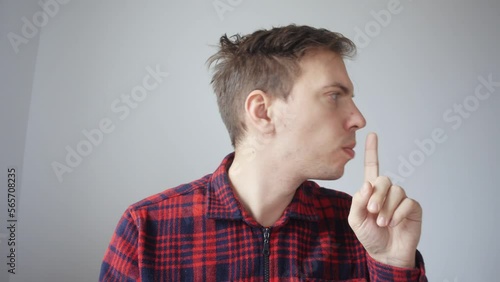 A young man participates in a business meeting online, a video conference via the Internet. A man shows someone behind the scenes a sign to be quiet.