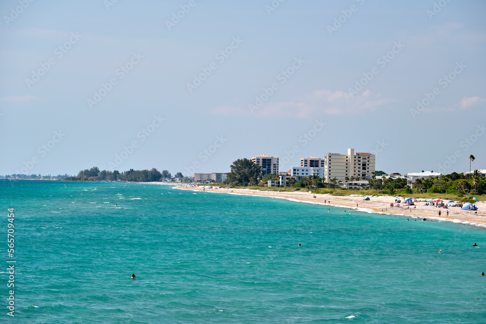 Resort beach with white sand, blue water, tall hotel buildings. Happy people sunbathing and swimming in ocean