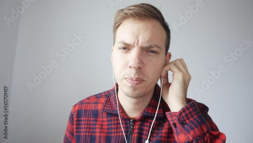 The man is trying to make out the speech in the wired headphones. A young man is talking on a video link. He does not hear the interlocutor, bad connection, unintelligible speech. Laptop webcam view.