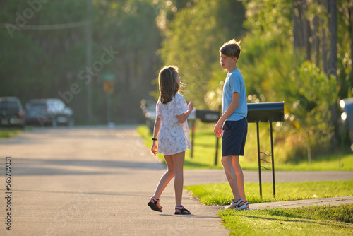 Two young teenage children, girl and boy standing and talking together outdoors on bright sunny day on rural street side © bilanol