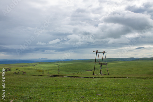 Beautiful landscape - electric poles with wires on a boundless green meadow in Karachay-Cherkessia and blue sky with white clouds and space for copying