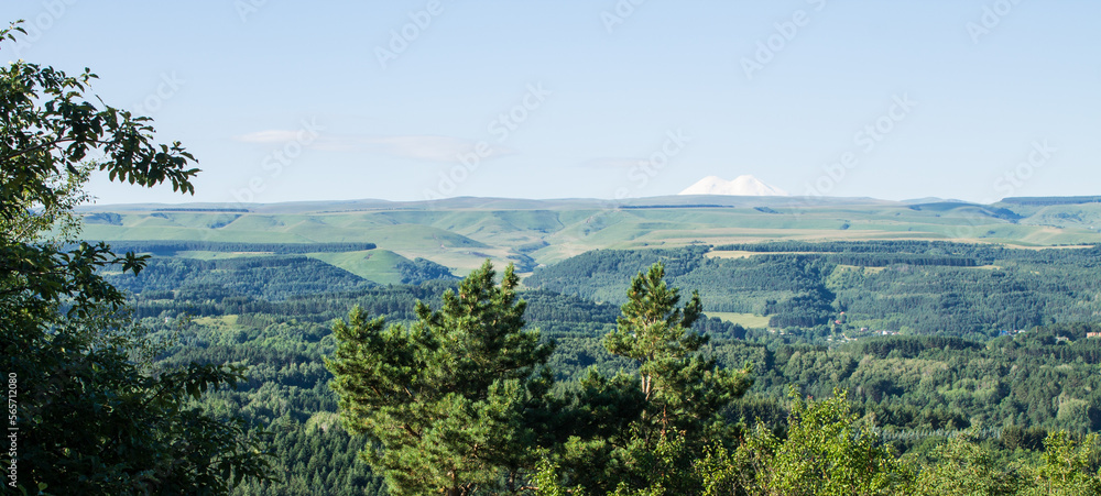 Panoramic view of the green valley and the snowy peak of Mount Elbrus against the blue clear sky on a sunny summer day and a space for copying in Russia in the Stavropol territory