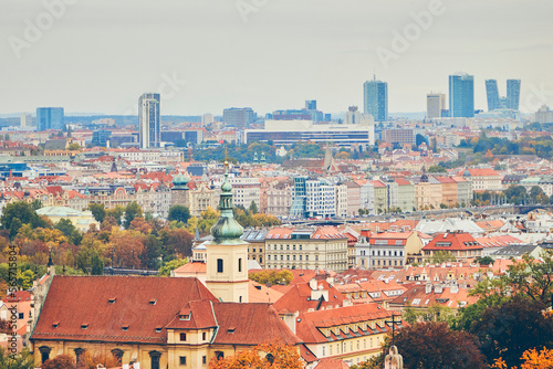 City view of Prague during autumn with traditional tile rooftops in foreground.